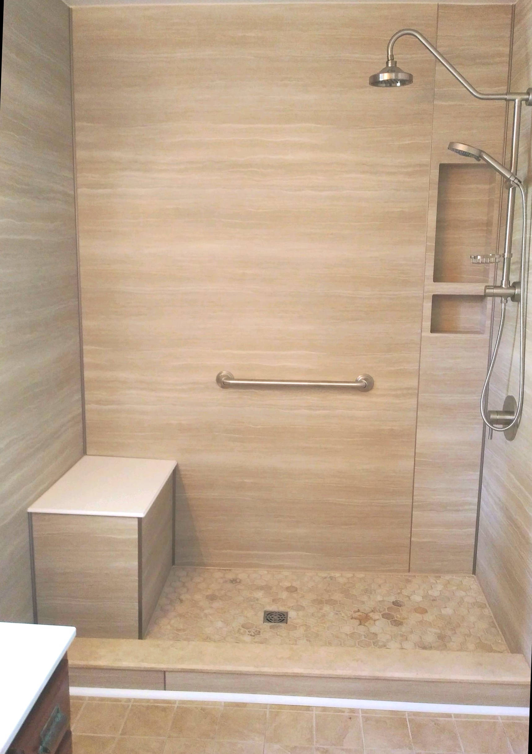 A walk in shower with a seat, grab bar, and built-in shelves