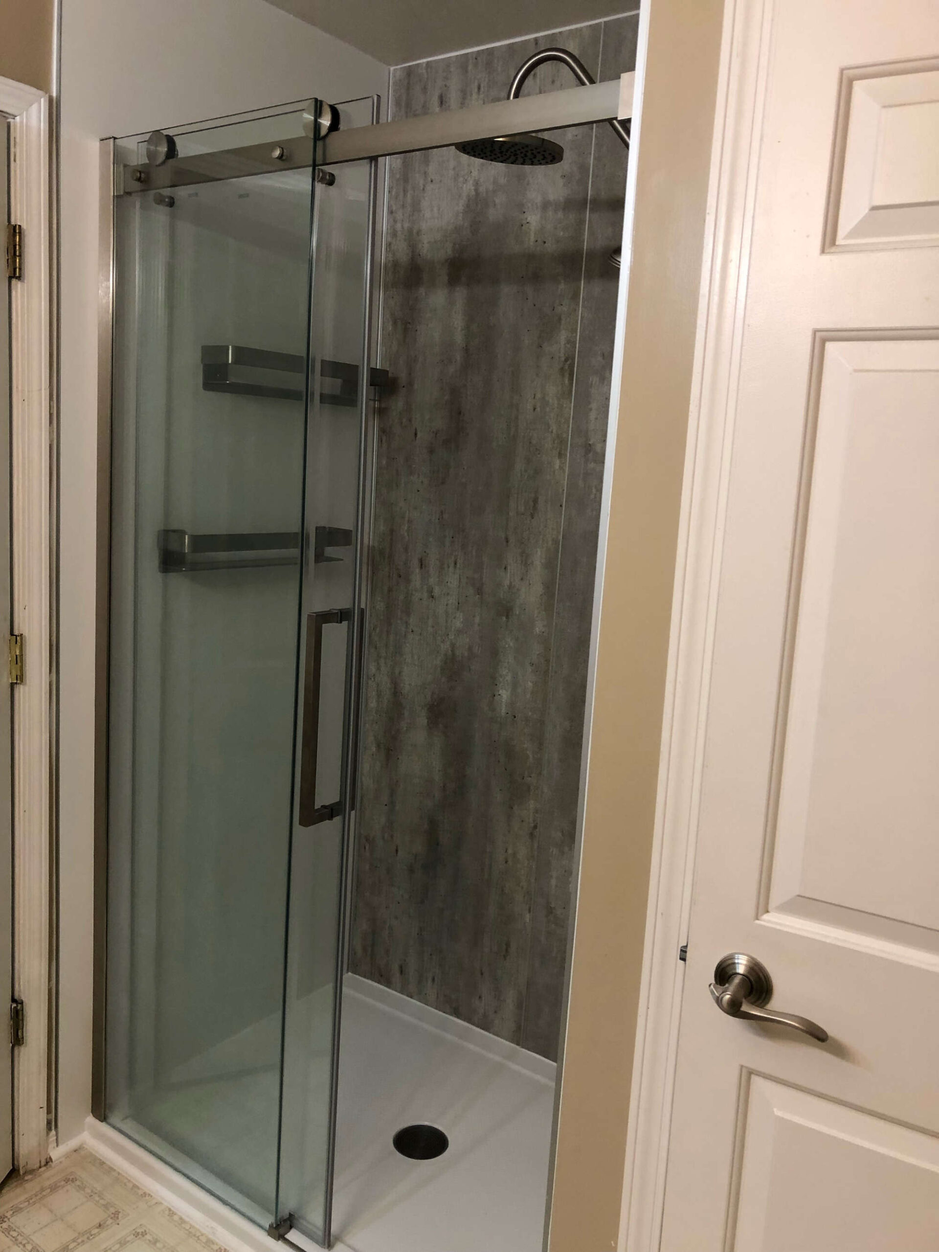 A small walk-in shower with a sliding glass door and center drain